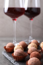 Photo of Tasty truffle bonbons and red wine on grey textured table, closeup