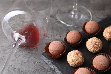 Photo of Tasty truffle bonbons and leftover red wine on grey textured table, closeup