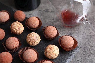 Photo of Tasty truffle bonbons and leftover red wine on grey textured table, closeup