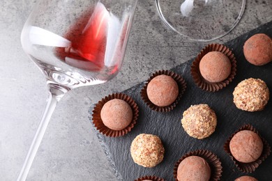 Photo of Tasty truffle bonbons and leftover red wine on grey textured table, flat lay