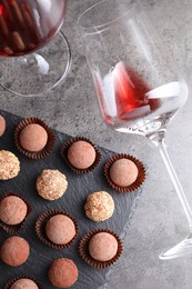 Photo of Tasty truffle bonbons and red wine on grey textured table, flat lay