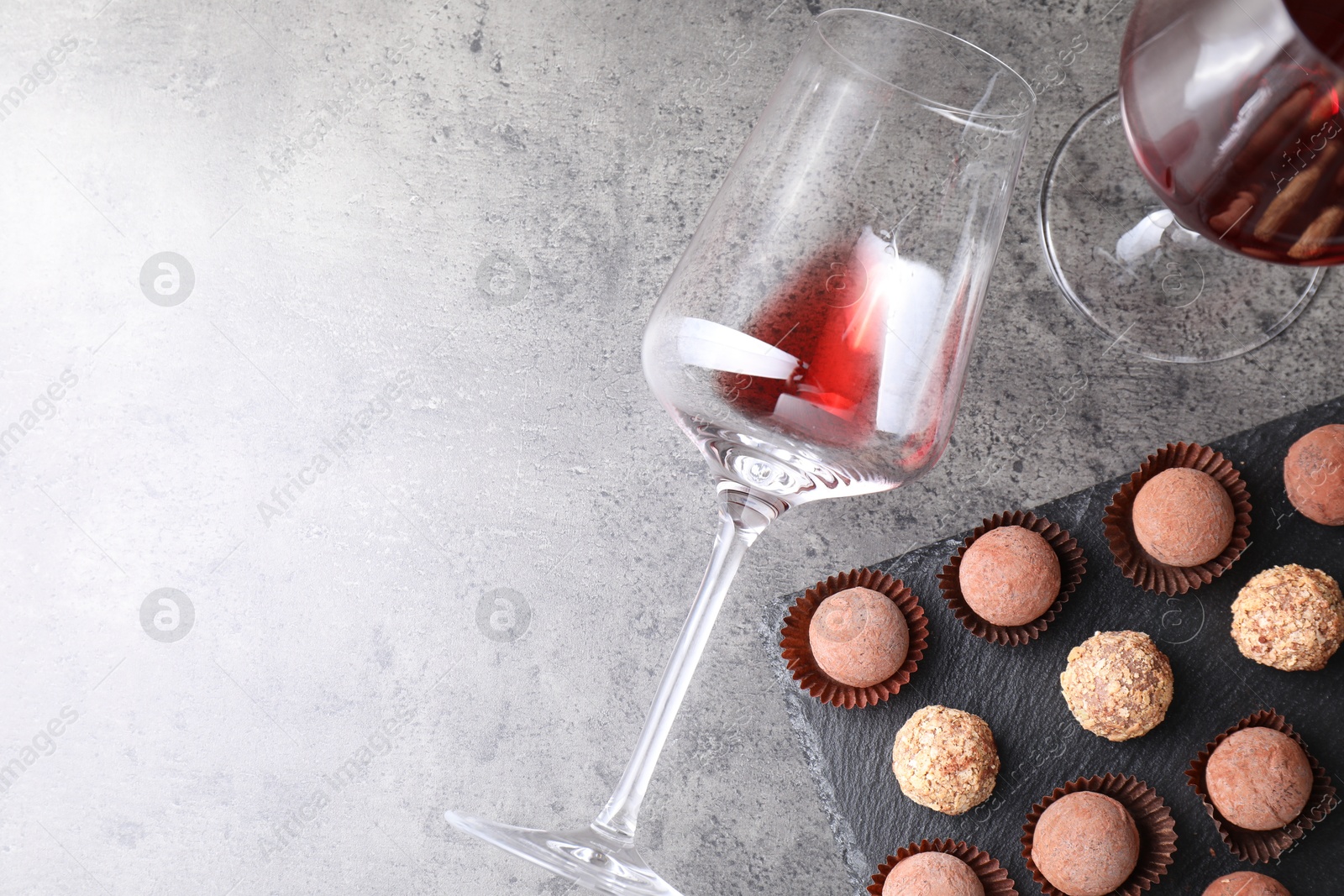 Photo of Tasty truffle bonbons and red wine on grey textured table, flat lay. Space for text