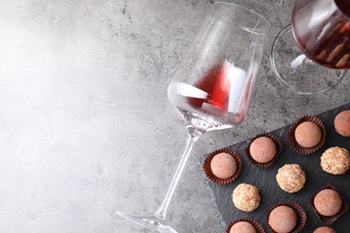 Photo of Tasty truffle bonbons and red wine on grey textured table, flat lay. Space for text