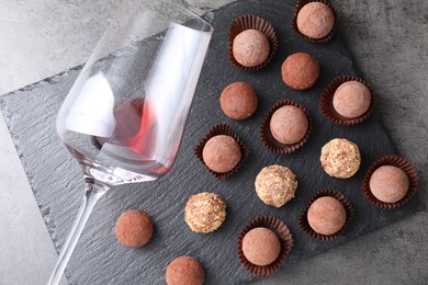 Photo of Tasty truffle bonbons and leftover red wine on grey textured table, top view