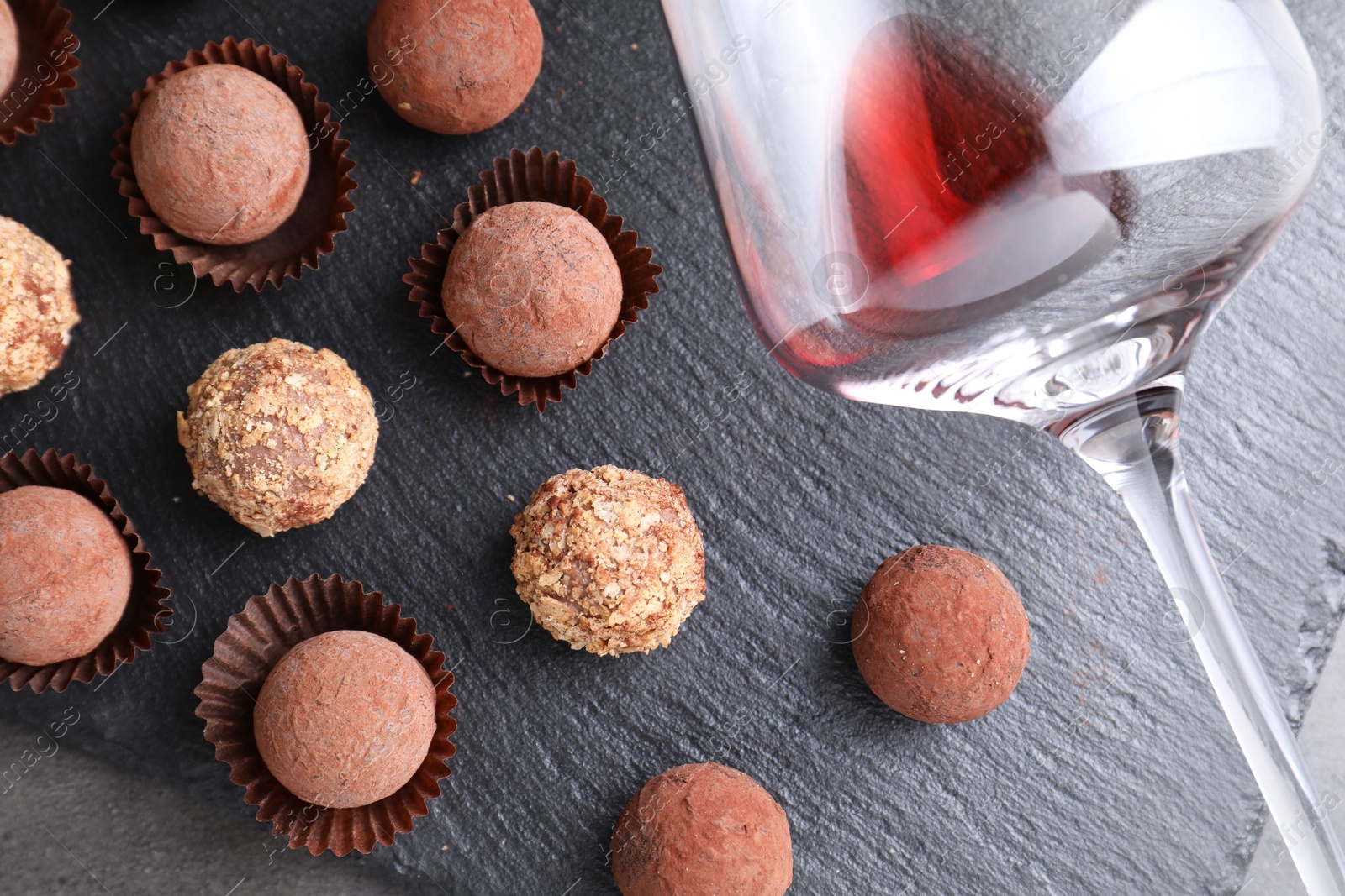 Photo of Tasty truffle bonbons and leftover red wine on grey textured table, top view