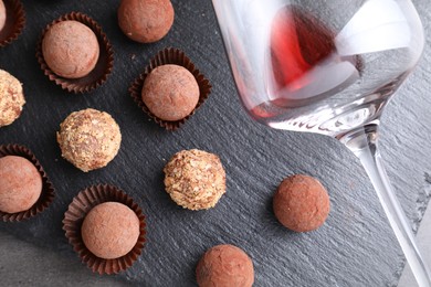 Photo of Tasty truffle bonbons and leftover red wine on grey textured table, top view