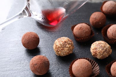 Photo of Tasty truffle bonbons and leftover red wine on dark textured table, closeup