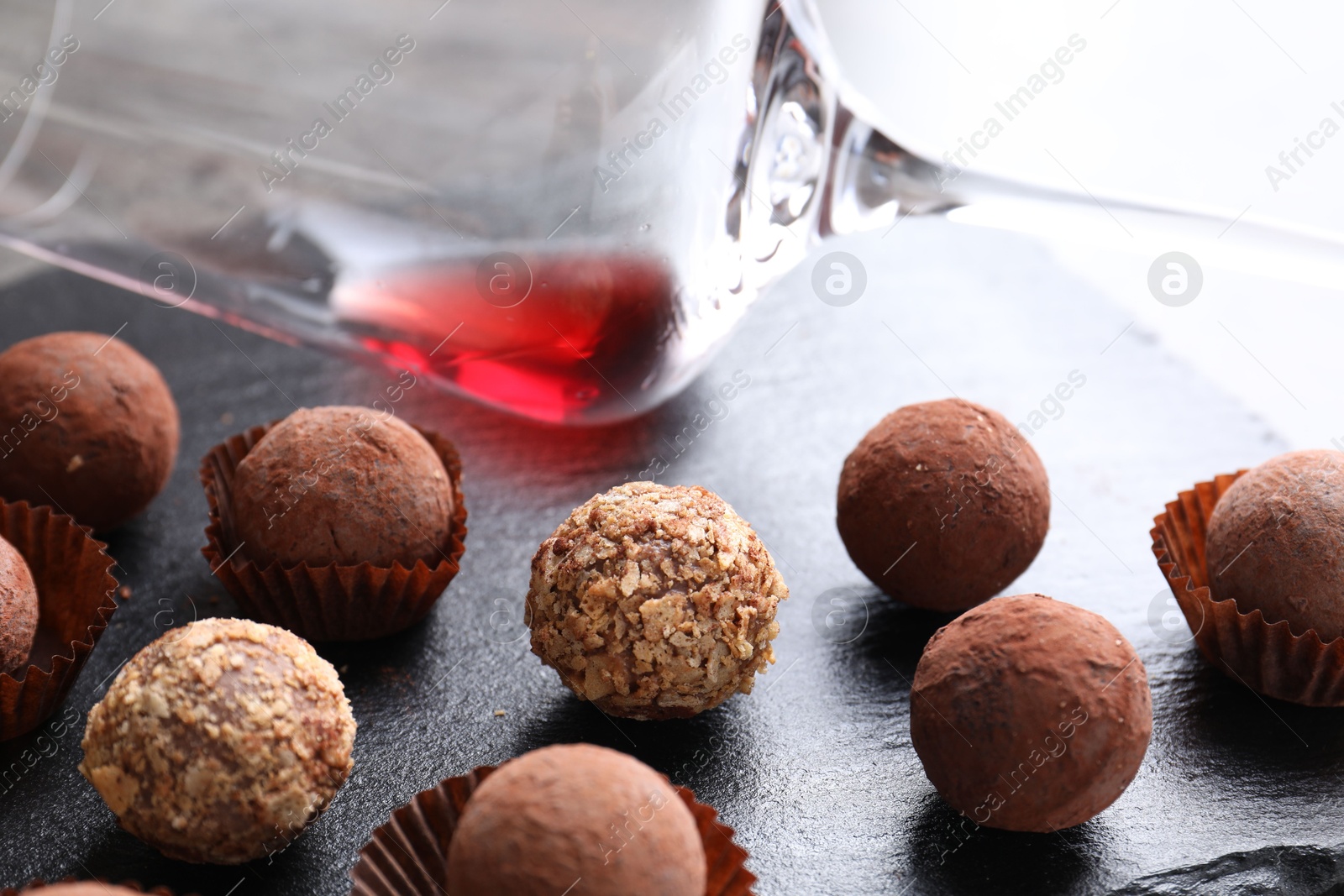 Photo of Tasty truffle bonbons and leftover red wine on dark textured table, closeup