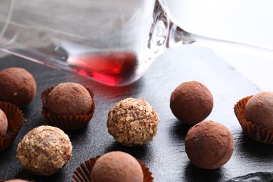 Photo of Tasty truffle bonbons and leftover red wine on dark textured table, closeup