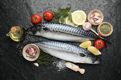 Photo of Fresh raw mackerels and spices on black table, flat lay. Seafood delicacies