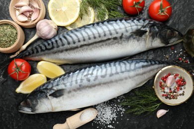 Photo of Fresh raw mackerels and spices on black table, flat lay. Seafood delicacies