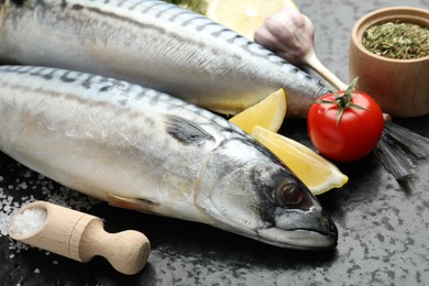 Photo of Fresh raw mackerels and spices on black table, closeup. Seafood delicacies