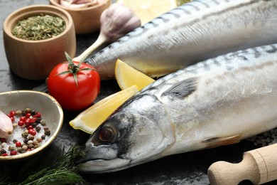 Photo of Fresh raw mackerels and spices on black table, closeup. Seafood delicacies