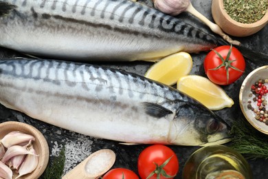 Photo of Fresh raw mackerels and spices on black table, flat lay. Seafood delicacies