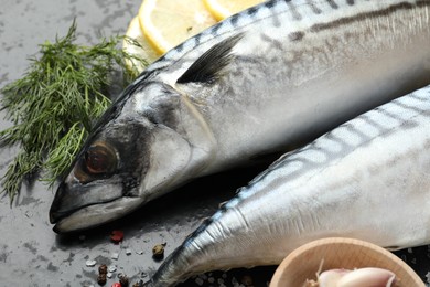 Photo of Fresh raw mackerels and spices on black table, closeup. Seafood delicacies