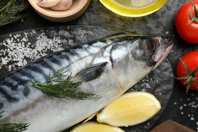 Photo of Fresh raw mackerel and spices on black table, flat lay. Seafood delicacies