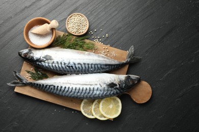 Photo of Seafood delicacies. Fresh raw mackerels and spices on black table, flat lay. Space for text