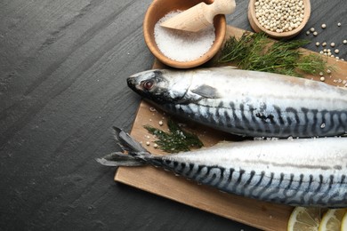 Photo of Seafood delicacies. Fresh raw mackerels and spices on black table, flat lay. Space for text