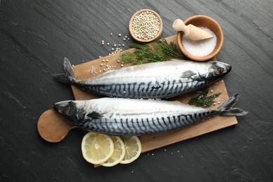 Photo of Fresh raw mackerels and spices on black table, flat lay. Seafood delicacies