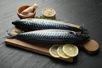 Photo of Fresh raw mackerels and spices on black table, closeup. Seafood delicacies