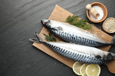 Photo of Seafood delicacies. Fresh raw mackerels and spices on black table, flat lay. Space for text