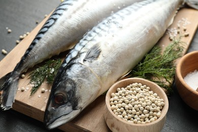Photo of Fresh raw mackerels and spices on black table, closeup. Seafood delicacies