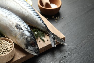 Photo of Seafood delicacies. Fresh raw mackerels and spices on black table, closeup. Space for text