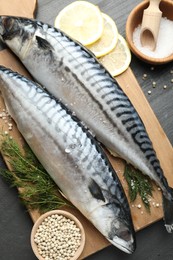 Photo of Fresh raw mackerels and spices on black table, flat lay. Seafood delicacies