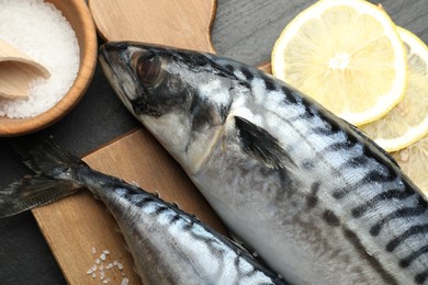Photo of Fresh raw mackerels and spices on black table, flat lay. Seafood delicacies