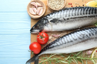 Photo of Seafood delicacies. Fresh raw mackerels and spices on light blue wooden table, flat lay. Space for text