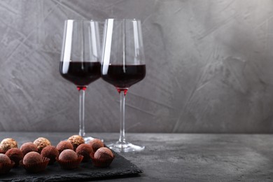 Photo of Tasty truffle bonbons and red wine on grey textured table, closeup. Space for text