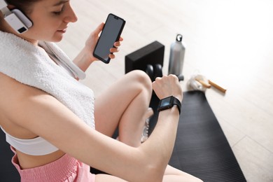 Photo of Woman checking fitness tracker during training indoors