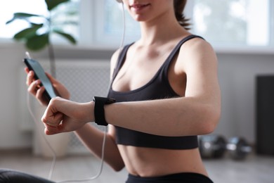 Photo of Woman checking fitness tracker during training indoors, closeup