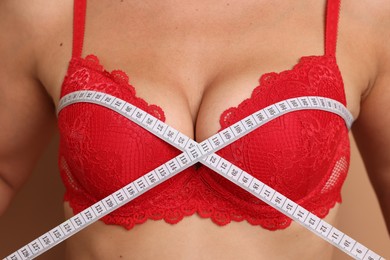 Photo of Woman in beautiful bra measuring breast circumference on beige background, closeup