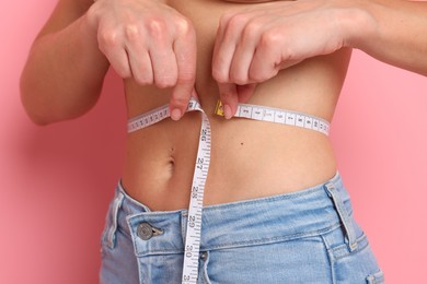 Photo of Woman measuring waist circumference on pink background, closeup