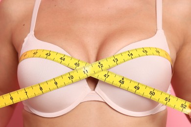 Photo of Woman in beautiful bra measuring breast circumference on pink background, closeup