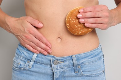 Photo of Gluten free diet. Woman with bun touching her belly on light grey background, closeup