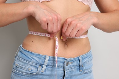 Photo of Woman measuring waist circumference on light grey background, closeup