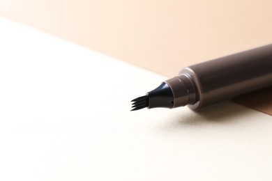 Photo of Brown liquid eyebrow pencil on beige background, closeup. Space for text