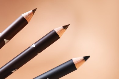 Photo of Different eyebrow pencils on beige background, closeup. Space for text