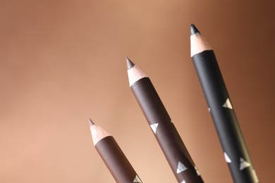 Photo of Different eyebrow pencils on beige background, closeup. Space for text
