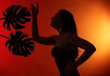 Photo of Silhouette of woman and tropical leaves on red gradient background