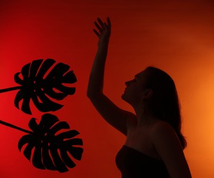 Photo of Silhouette of woman and tropical leaves on red gradient background