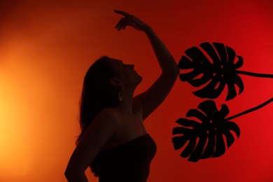 Photo of Silhouette of woman and tropical leaves on red gradient background