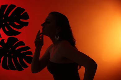 Photo of Silhouette of woman and tropical leaves on red gradient background