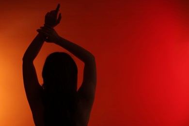 Photo of Silhouette of woman posing on red gradient background, back view. Space for text