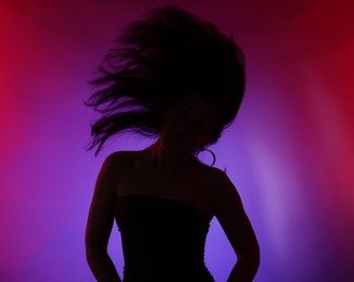Photo of Silhouette of woman posing in neon lights on color background
