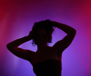 Photo of Silhouette of woman posing in neon lights on color background