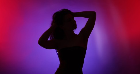 Photo of Silhouette of woman posing in neon lights on color background
