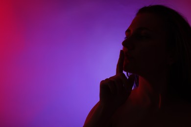 Photo of Silhouette of woman making silent gesture in neon lights on color background, space for text